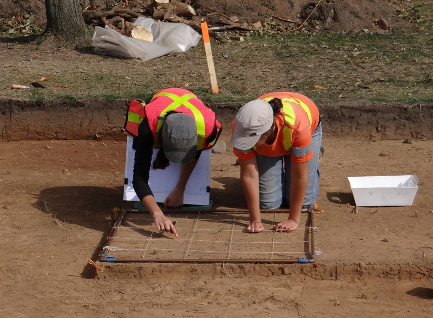 Two archaeologists working together to map in artifacts using a grid