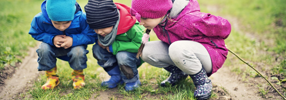 Three children examining the ground outdoors
