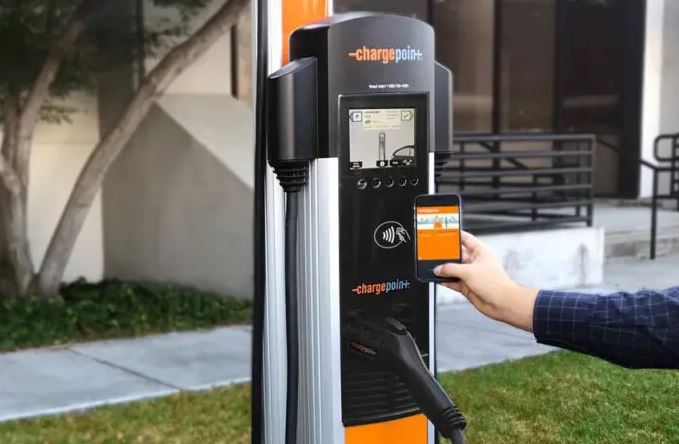 Hand holding a cell phone to a ChargePoint EV charging station