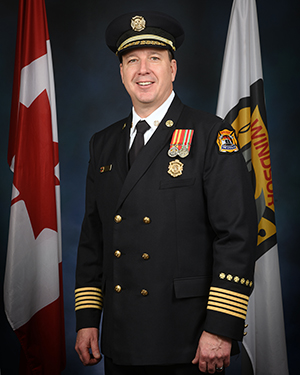 Fire Chief James Waffle in formal uniform flanked by flags of Canada and Windsor Fire & Rescue Services