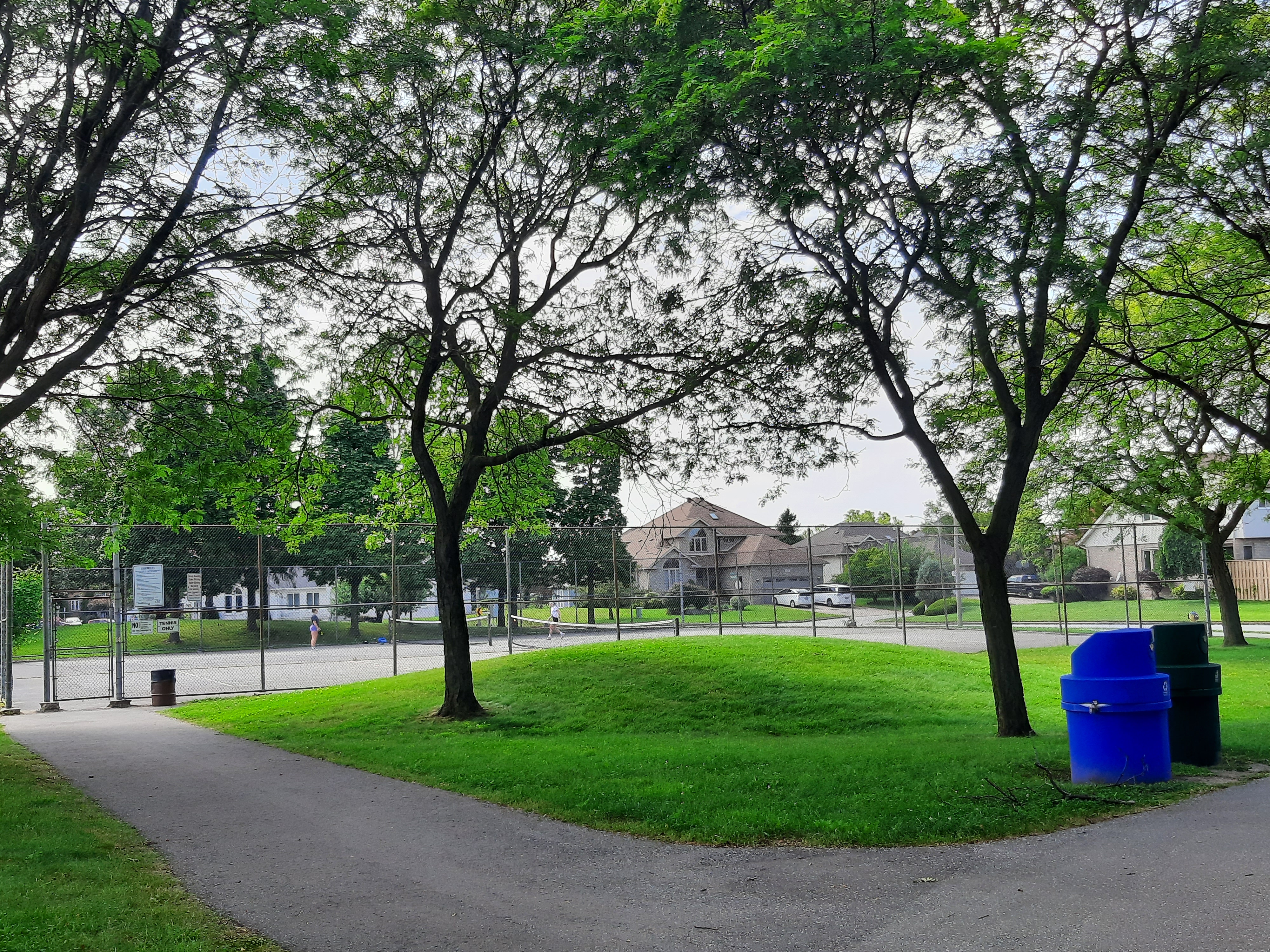 Pathway, small grassy hill and fenced tennis courts