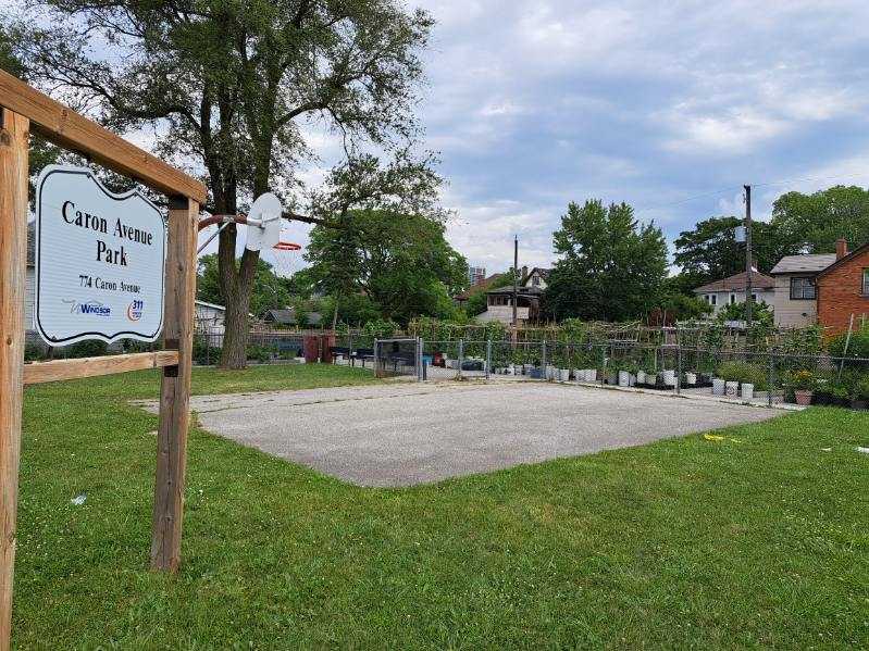 Caron Avenue Park sign and basketball key with community garden in the background