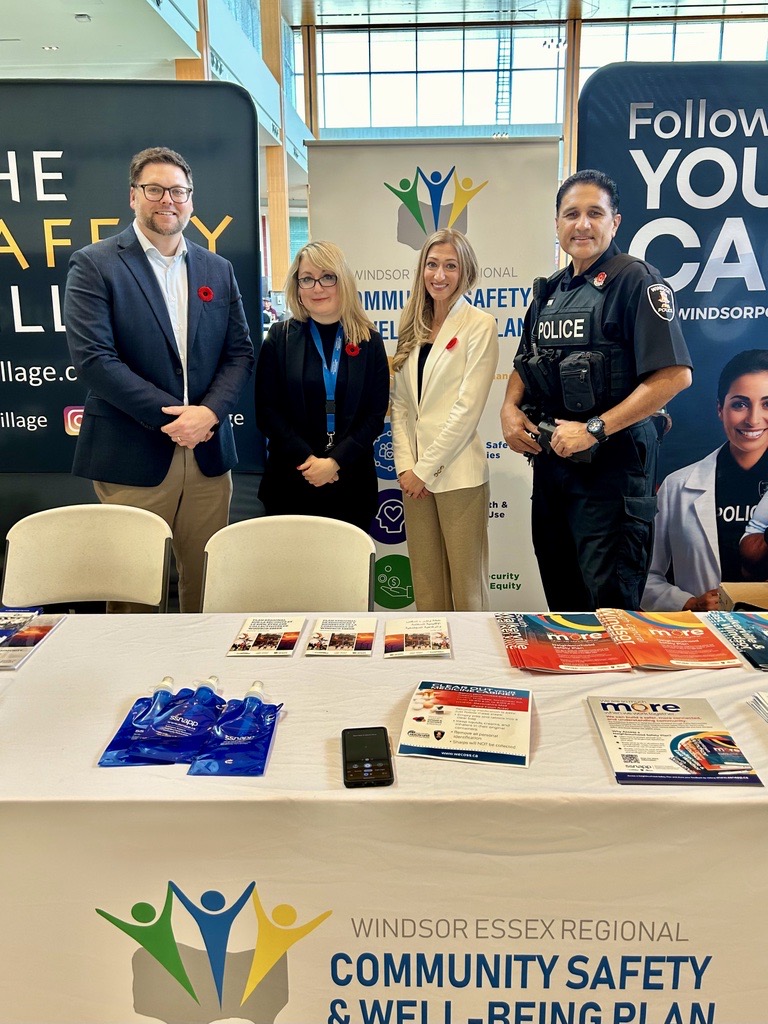 Participants, including a police officer,, gathered around a Windsor Essex Regional Community Safety & Well-Being Plan information booth at Devonshire Mall